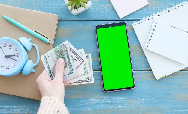 mobile-phone-with-green-screen-laptop-money-as-wooden-background_