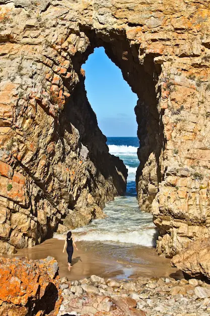 vertical-shot-female-standing-front-cave-leading-ocean_181624-11731